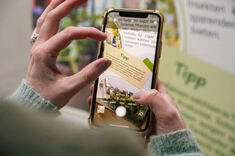 Ein Smartphone fotografiert einen Auschnitt eines Rollup der Ausstellung Vielfalt im Garten